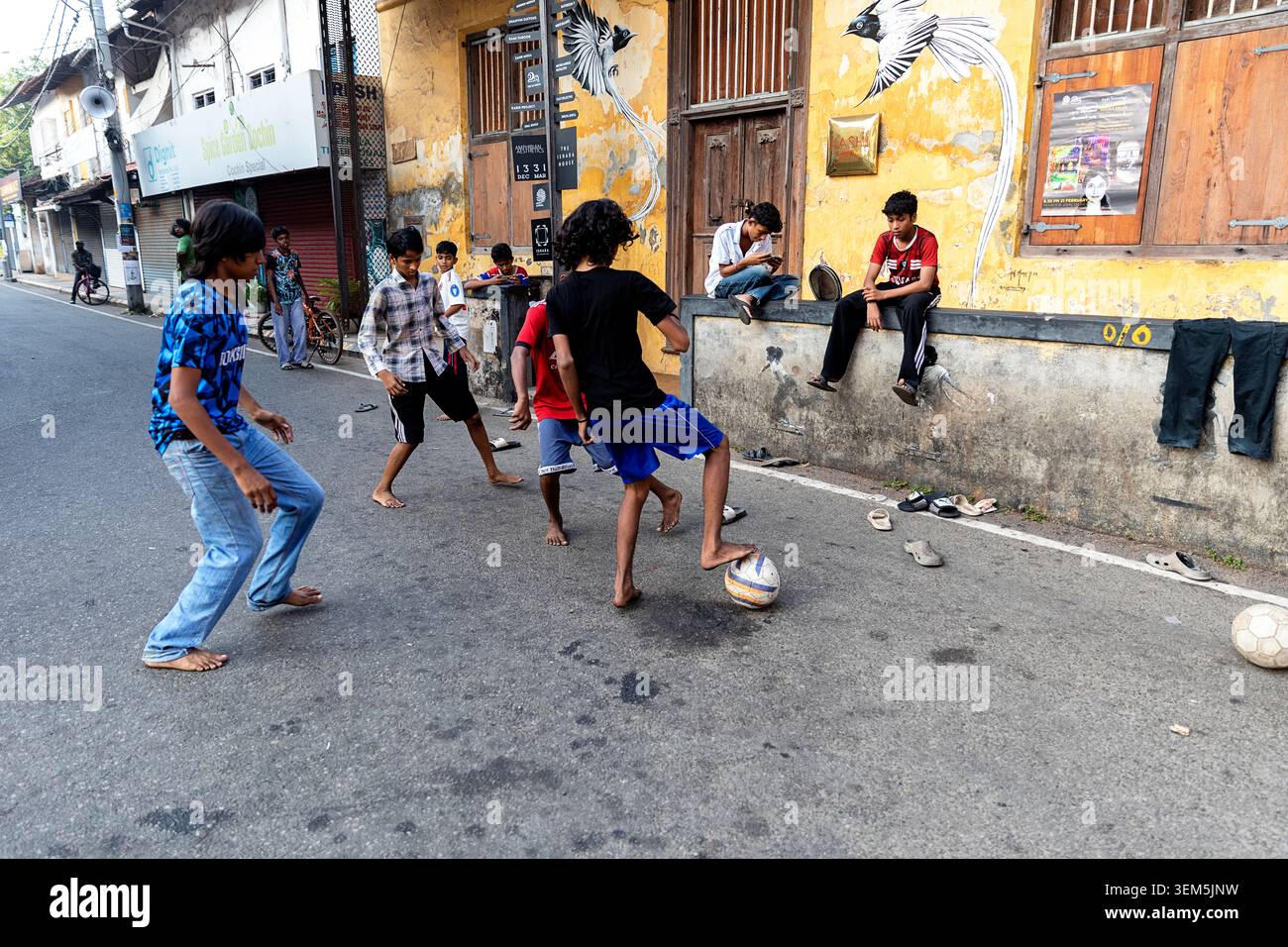 Un gruppo di ragazzi che giocano a football di strada di fronte a un colorato edificio murale nello storico quartiere di Jew Town, Kochi, Kerala, India Foto Stock