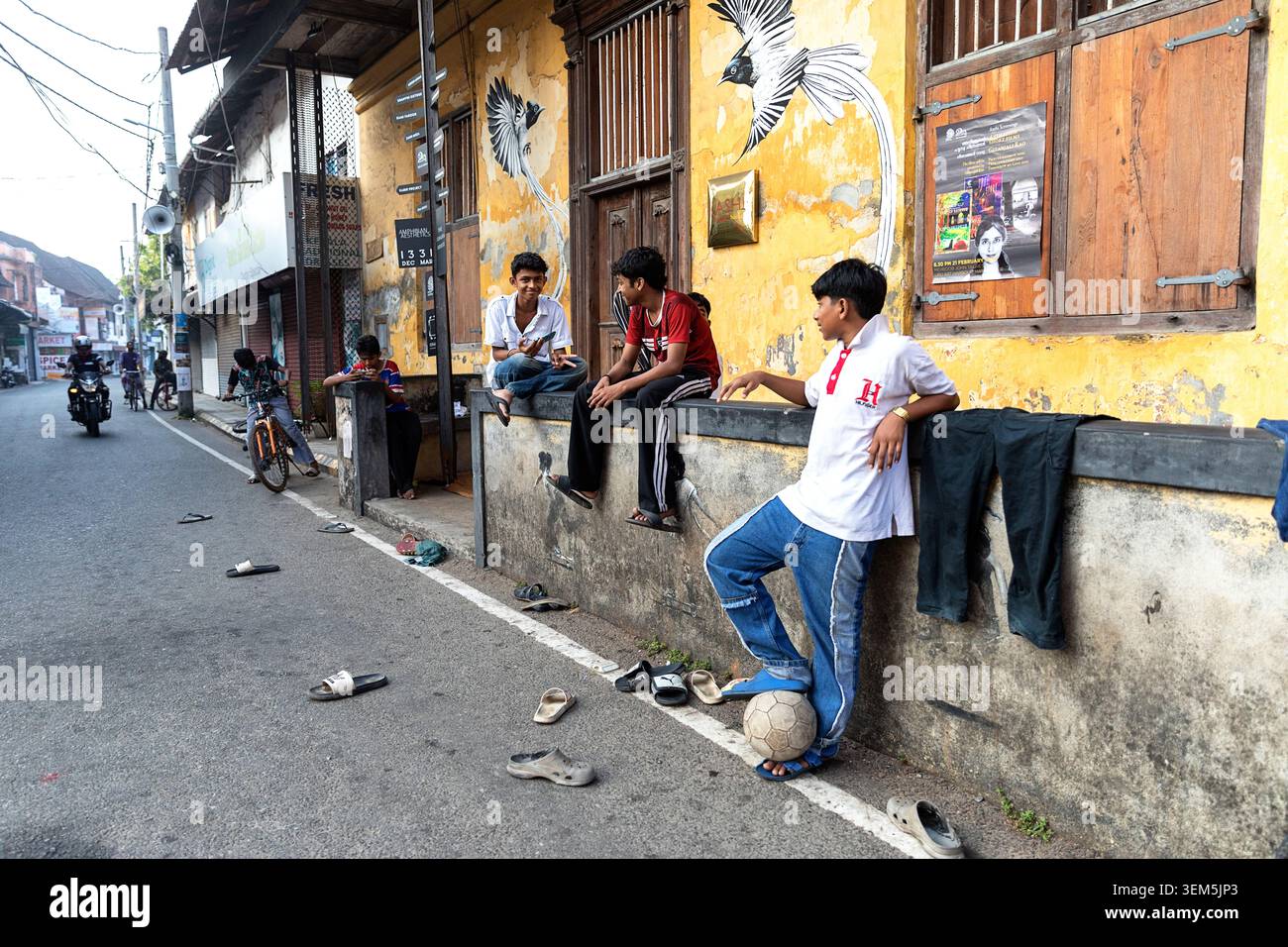 Un gruppo di ragazzi che giocano a football di strada e si riposano durante una partita di fronte a un edificio colorato nel quartiere di Jew Town a Kochi, Kerala, India Foto Stock