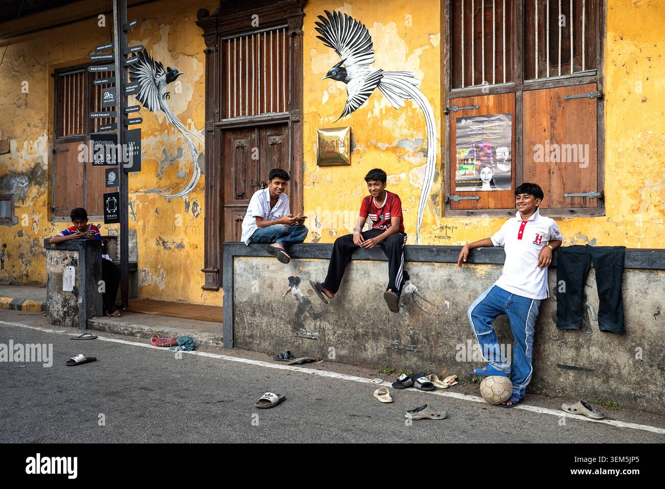 Un gruppo di ragazzi che giocano a football di strada e si riposano durante una partita di fronte a un edificio colorato nel quartiere di Jew Town a Kochi, Kerala, India Foto Stock