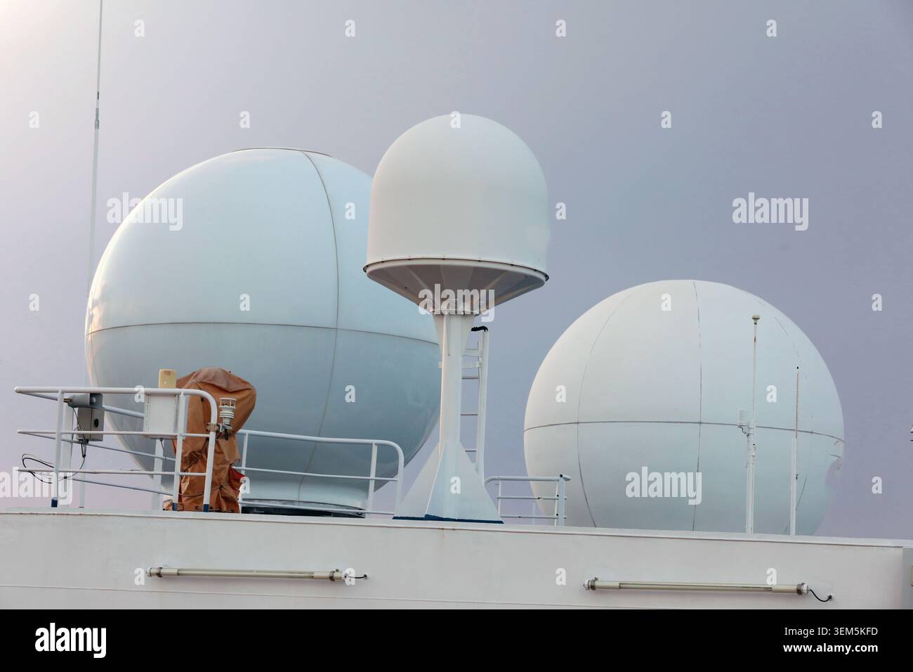 Radomi sferici bianchi e sistemi di comunicazione a cupola satellitare montati sul ponte superiore di navigazione di una nave passeggeri contro una S rovesciata Foto Stock