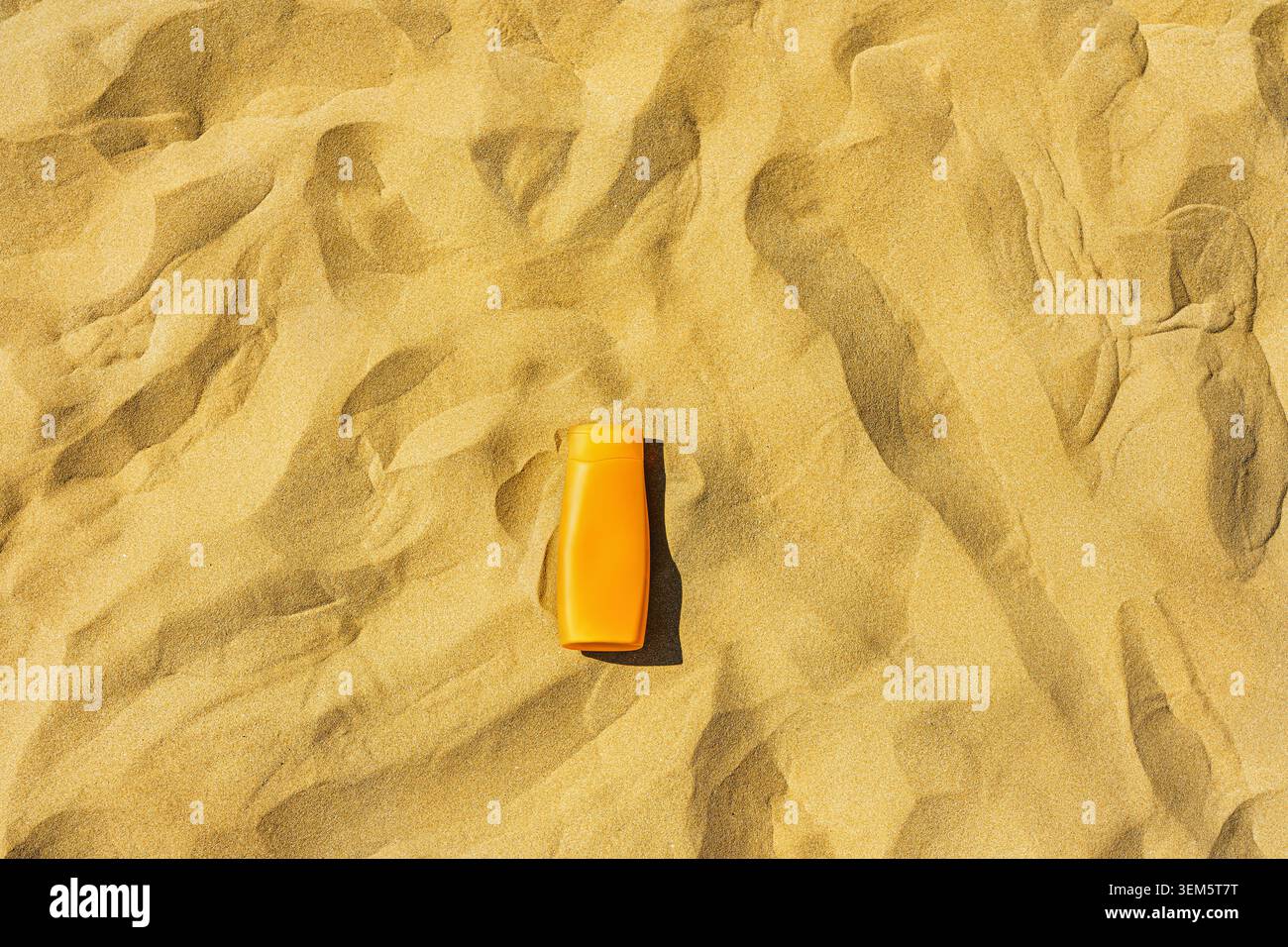 Crema solare - Una bottiglia di crema solare senza logo adagiato sullo sfondo di sabbia. Foto Stock