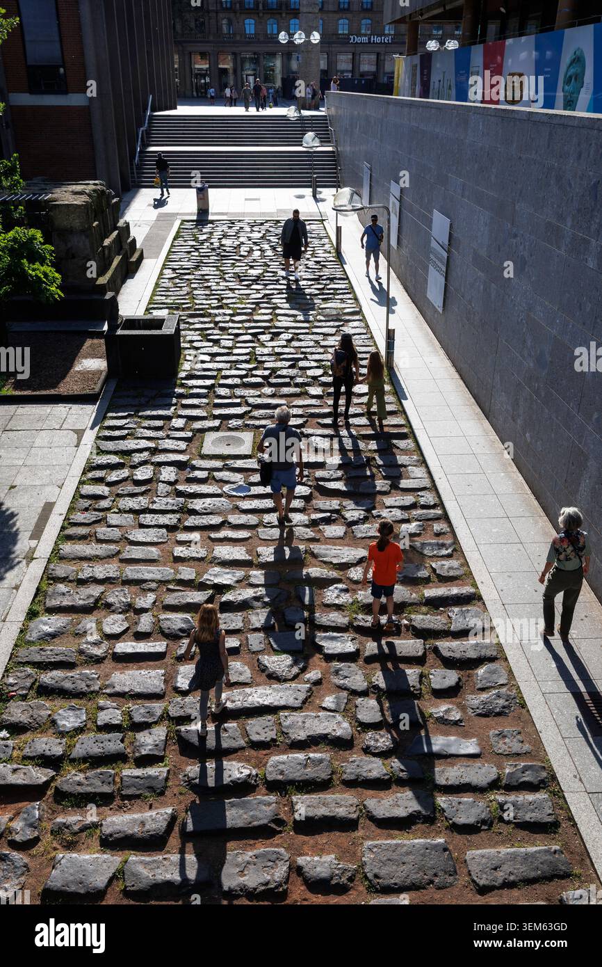 Persone che camminano sulla vecchia strada del porto romano vicino alla cattedrale, Colonia, Germania. Menschen gehen ueber die alte roemische Hafenstrasse nahe Dom, K. Foto Stock