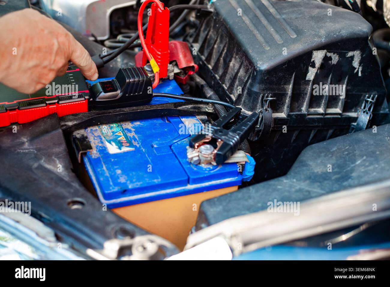 Le mani di una persona collegano i cavi di collegamento a una batteria blu per auto. manutenzione automobilistica, riparazione veicoli, emergenza stradale. Foto Stock