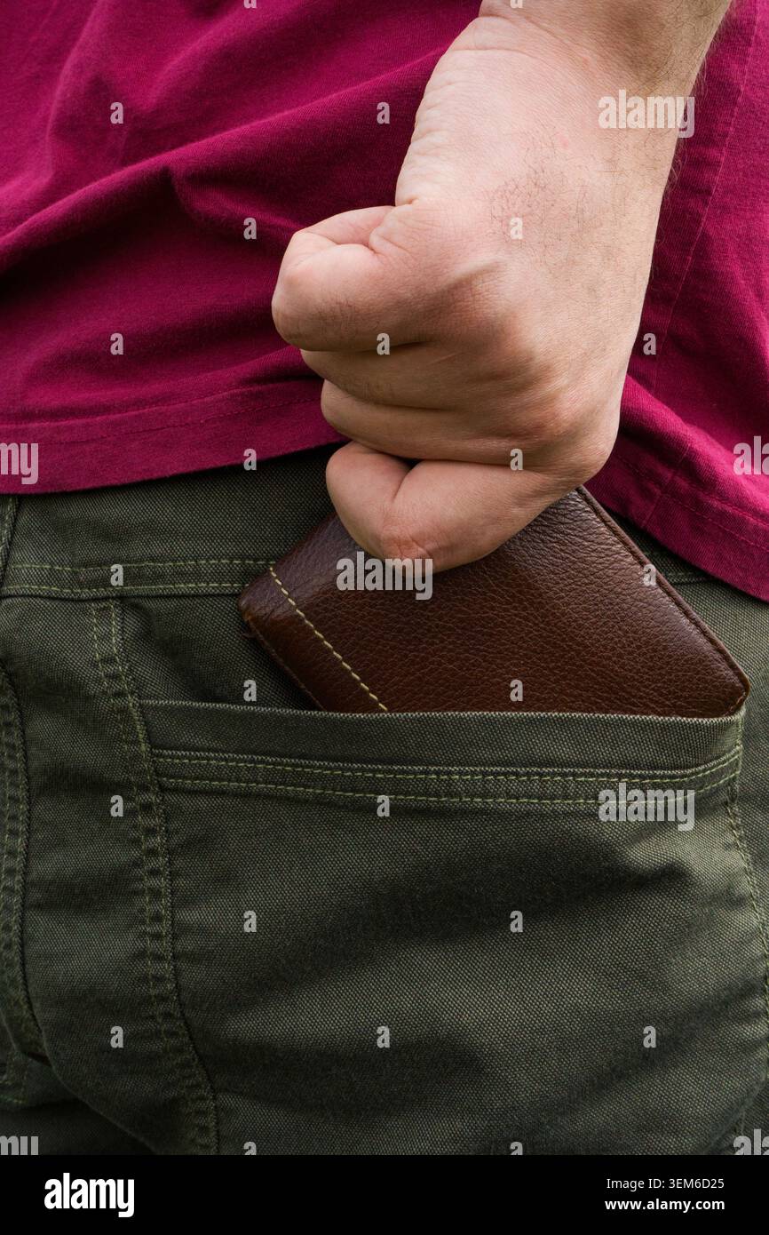 Primo piano della mano di un uomo che mette un portafoglio marrone in pelle in una tasca posteriore, una borsa personale e un concetto di trasporto quotidiano. Foto Stock