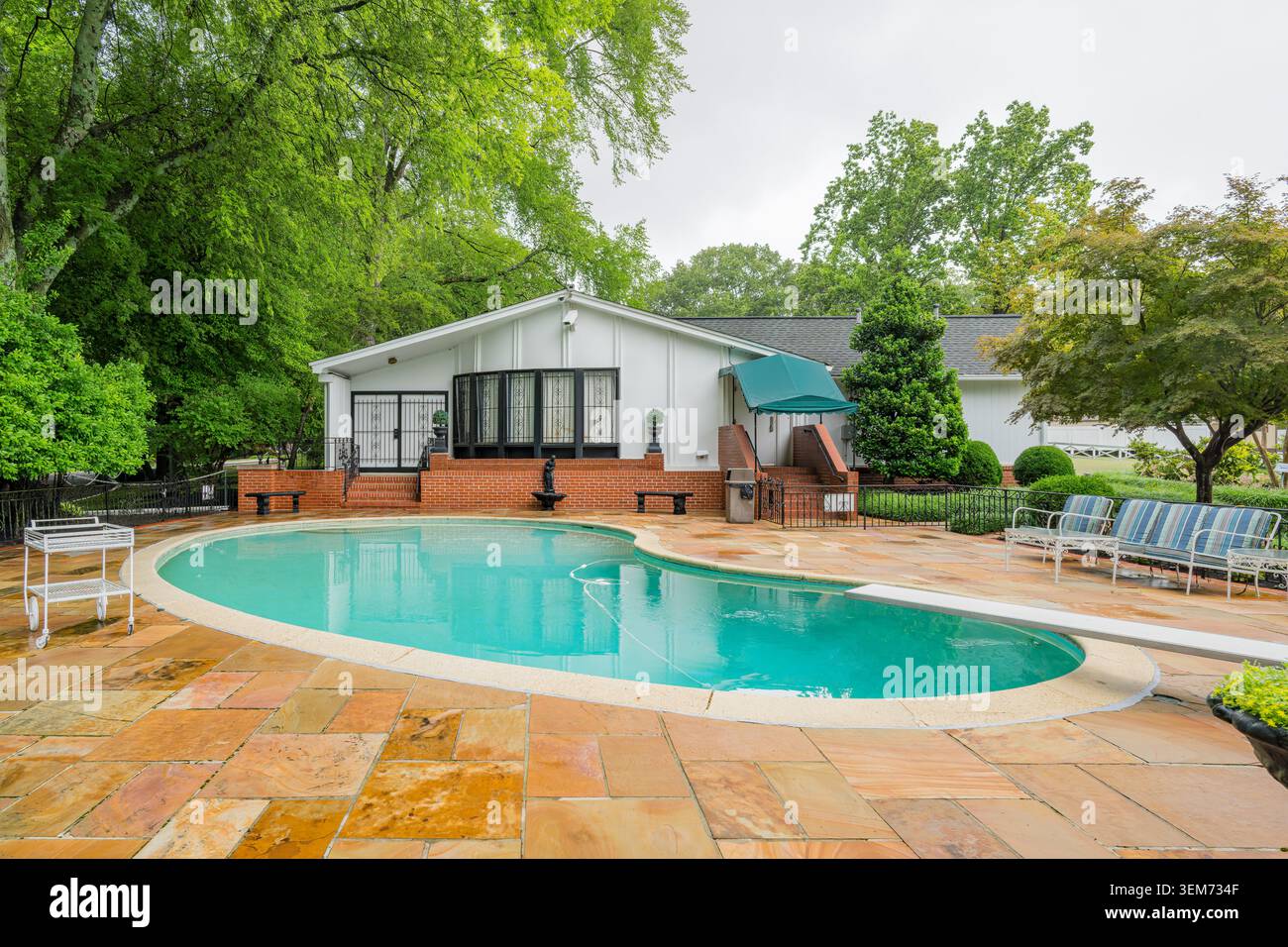 Memphis, Stati Uniti, 24 MAGGIO 2026 - Una piscina a forma di rene con acqua turchese è circondata da un patio in pietra e una casa della piscina bianca con Foto Stock