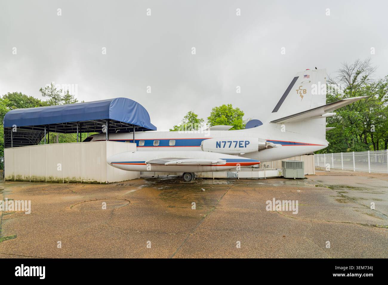 Memphis, Stati Uniti, 24 MAGGIO 2026 - Un jet privato bimotore bianco con strisce blu e rosse è fermo su una piattaforma di cemento bagnata accanto a un tendone blu Foto Stock