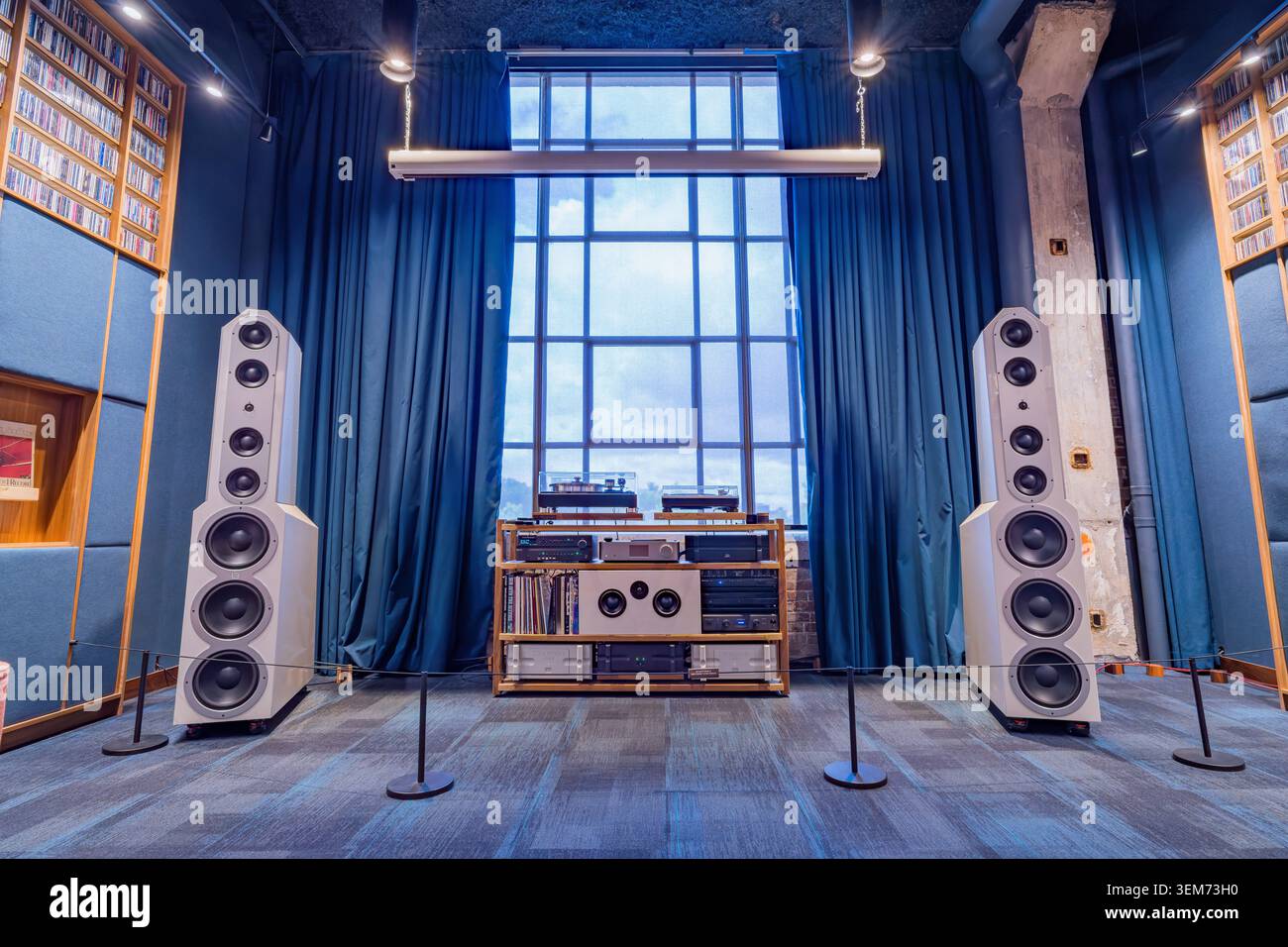 Memphis, Stati Uniti, 24 MAGGIO 2026 - Due grandi altoparlanti bianchi a pavimento fiancheggiano una rastrelliera in legno di apparecchiature audio in una stanza con pareti blu e un Foto Stock