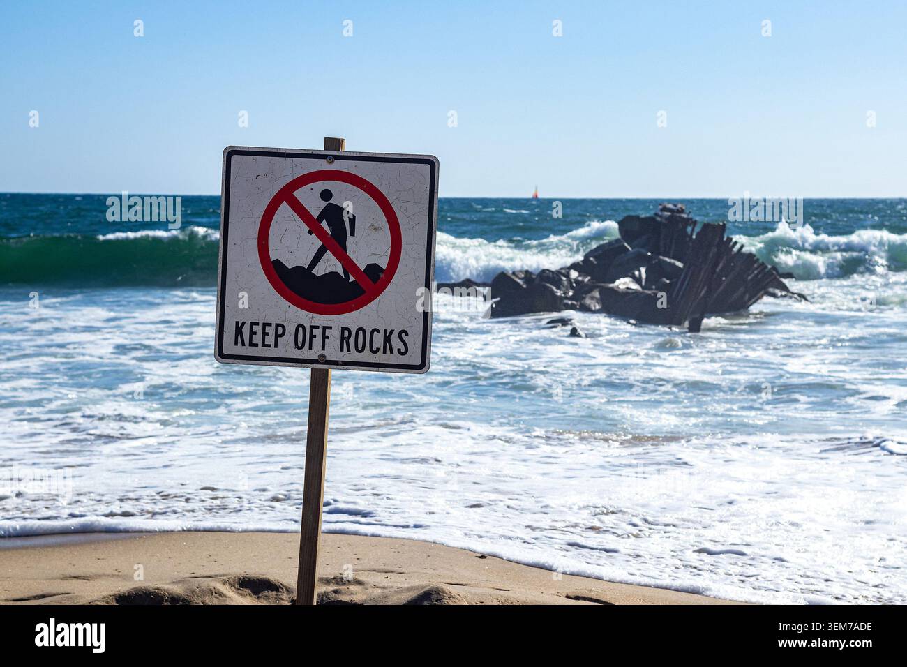 Cartello Keep Off Rocks sulla spiaggia, con rocce nell'oceano sullo sfondo, segnali di sicurezza, avviso di pericolo sulla riva Foto Stock