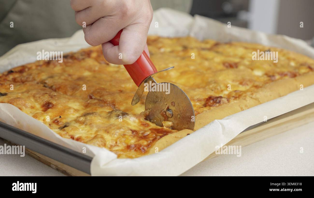 Tagliare la pizza con un coltello rotondo. Primo piano della deliziosa pizza tagliata a pezzi. Affettare al rallentatore una pizza in più fette con una cu Foto Stock