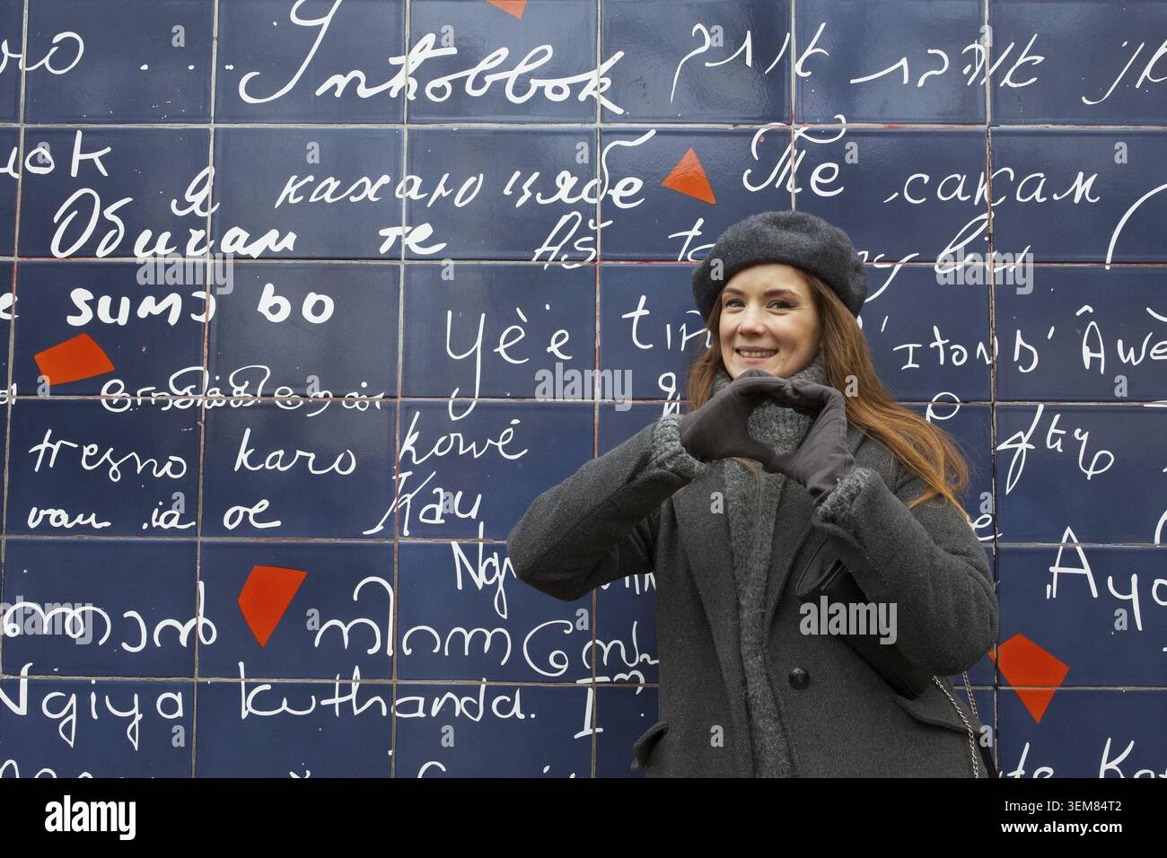 Una donna allegra in abito invernale forma un cuore con le mani di fronte al famoso muro dell'amore (le Mur des Je taime) a Montmartre, Parigi Foto Stock
