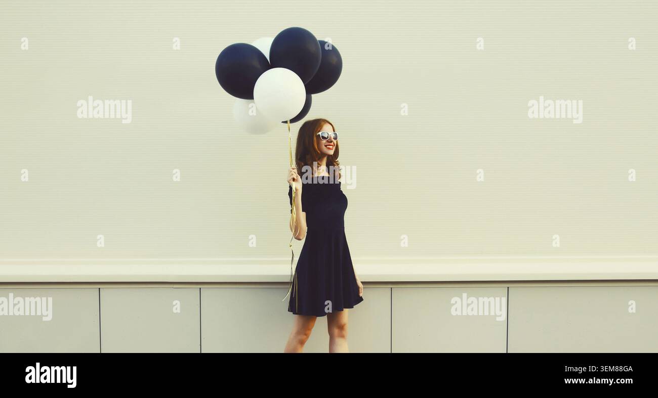 Eine froehliche junge Frau mit einem Strauss schwarz-weisser Luftballons in der Stadt Foto Stock