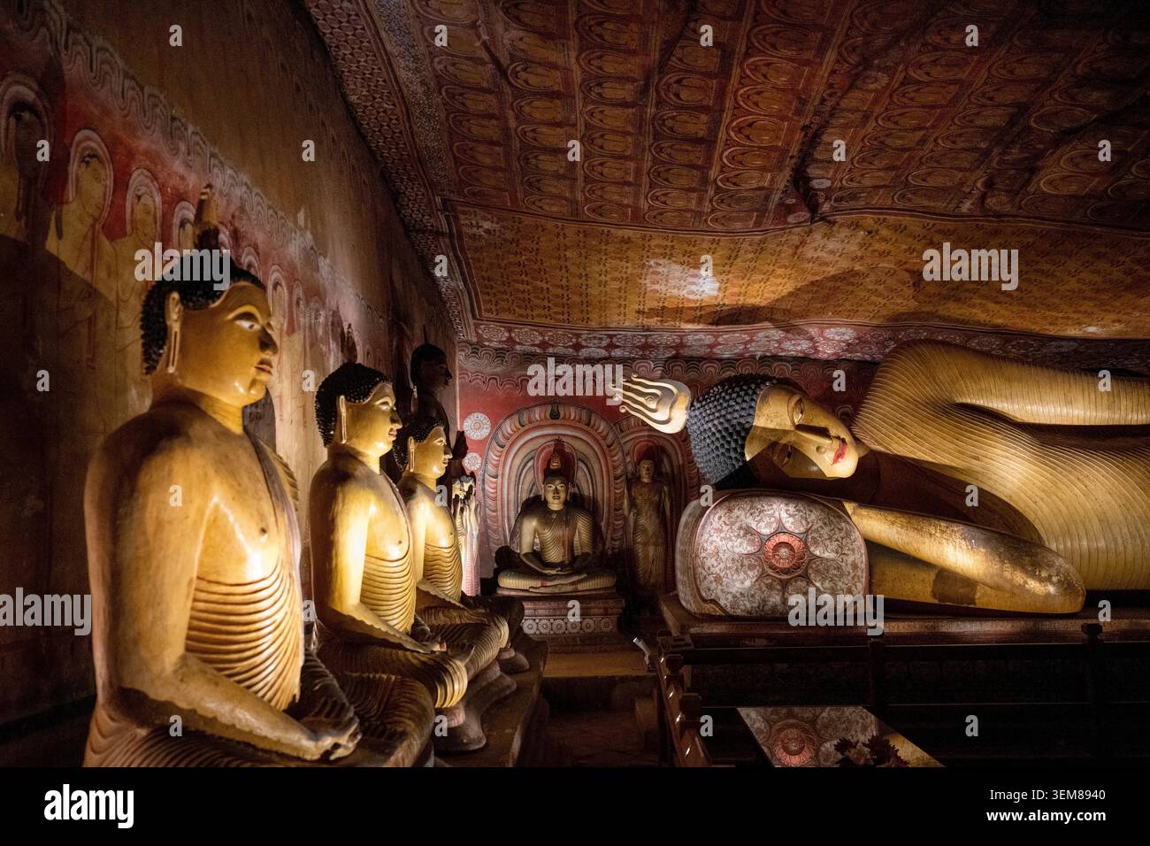 Vista laterale di una monumentale statua di Buddha sdraiato scavata nella roccia, circondata da antichi affreschi nel Tempio delle Grotte di Dambulla. Foto Stock