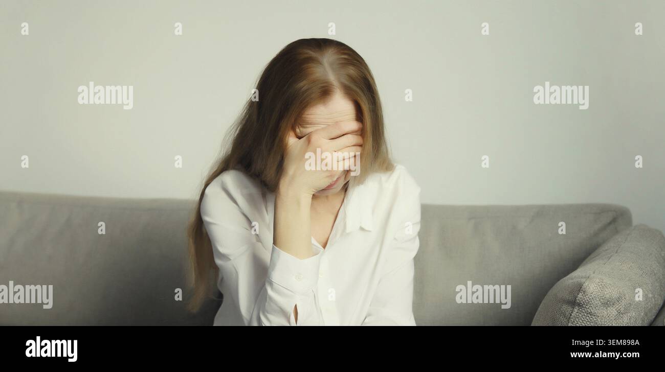 Donna stanca e stanca che tocca la testa, soffre di mal di testa, stress, affaticamento, dolore ai templi, emicrania, rumore forte, tensione seduta sul divano a hom Foto Stock