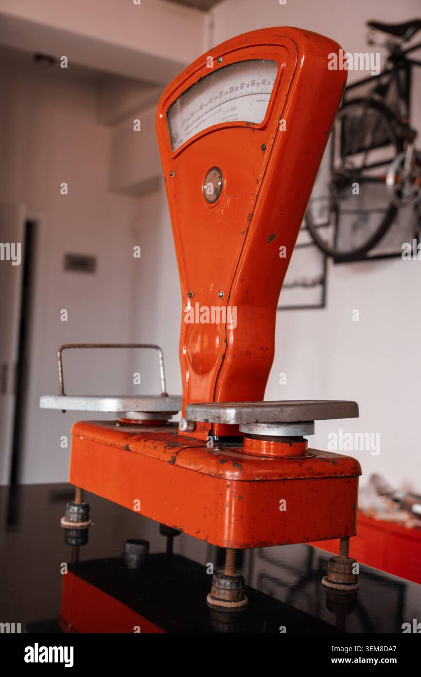 Primo piano dettagliato di una bilancia meccanica rossa vintage con superfici metalliche usurate e display analogico classico. Simbolo di attrezzature per la vendita al dettaglio di oggetti d'antiquariato Foto Stock