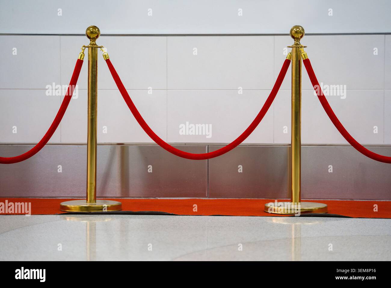 I montanti in metallo oro e una corda di velluto formano un sentiero sul tappeto rosso vicino alla parete piastrellata per organizzare le code all'ingresso del cinema. Foto Stock