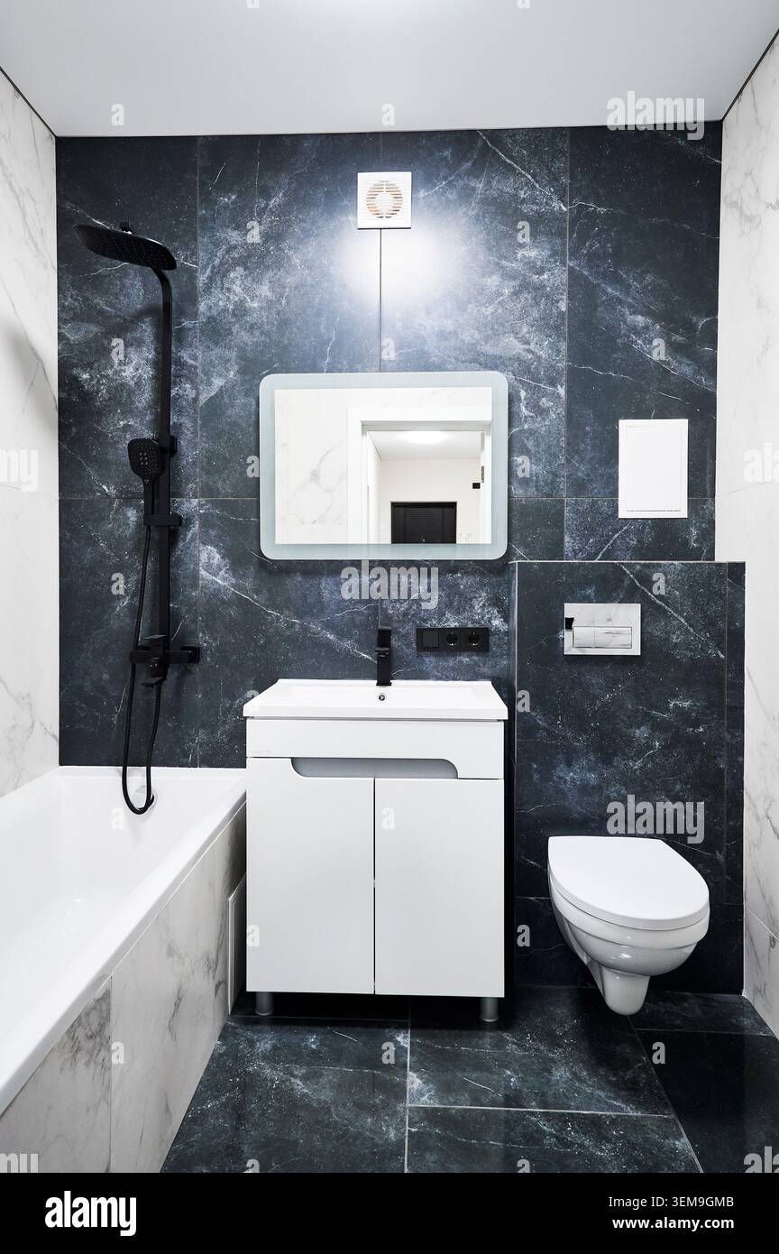 Bagno dal design contemporaneo con WC galleggiante, lavandino bianco e vasca. Bagno elegante con profonde pareti in grafite, accenti in marmo ed eleganti finiture nere Foto Stock