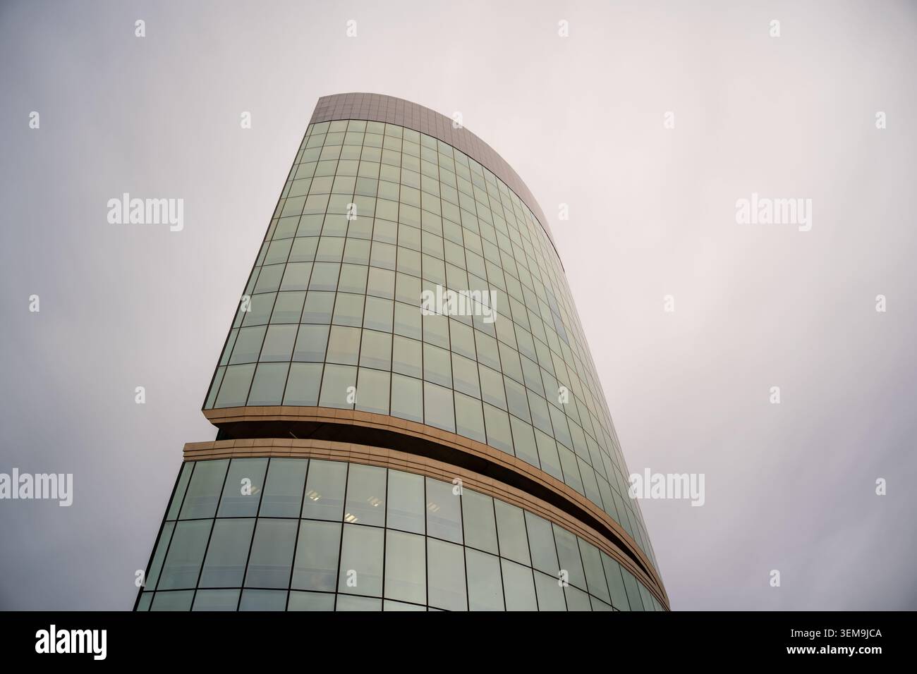 Moderno edificio in vetro che si piega verso l'alto contro un semplice cielo grigio Foto Stock