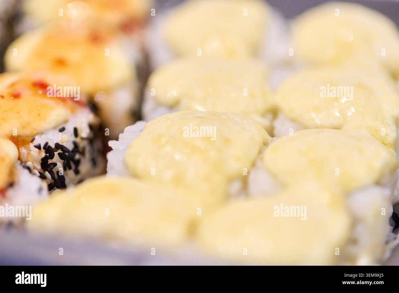 Vista macro dei panini di sushi makizushi conditi con salsa cremosa e semi di sesamo nero su sfondo neutro con toni tenui e luminosi che si concentrano sul sushi anteriore Foto Stock