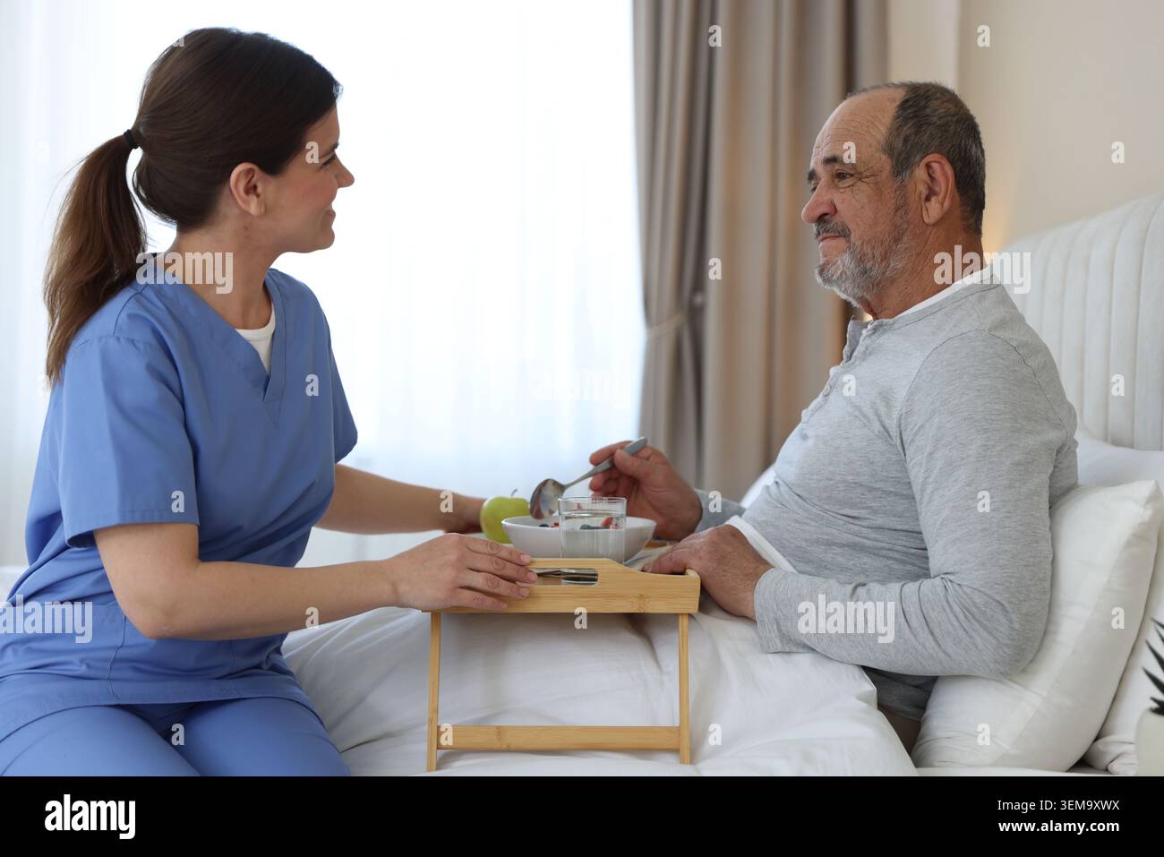 Assistente che fa colazione a un anziano a letto a casa Foto Stock