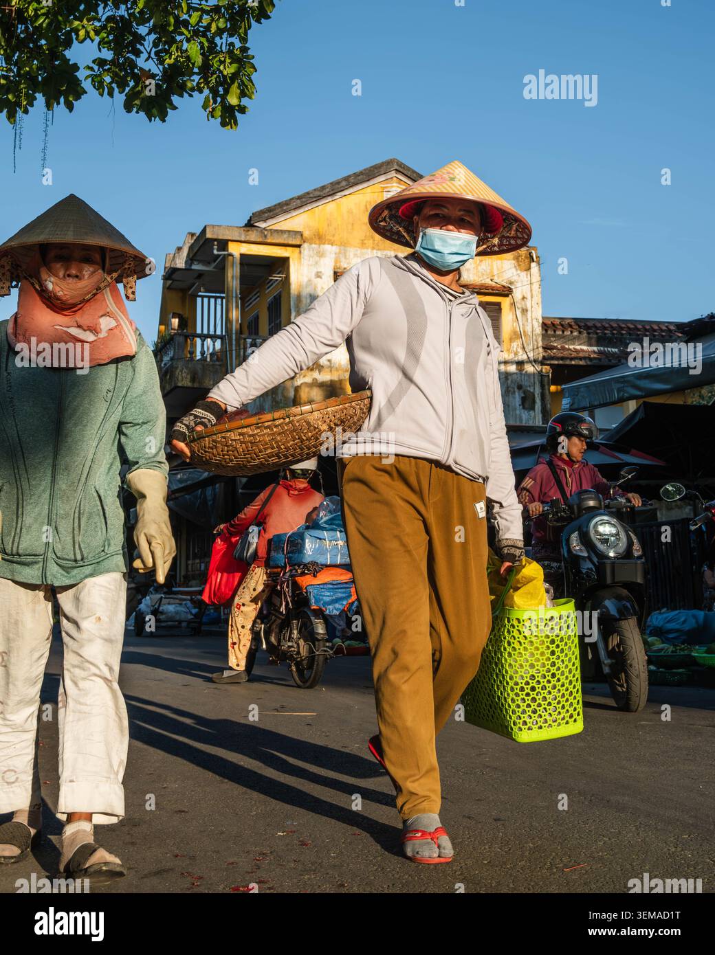 Venditori di strada vietnamita che trasportano cesti davanti a un vecchio edificio giallo Foto Stock