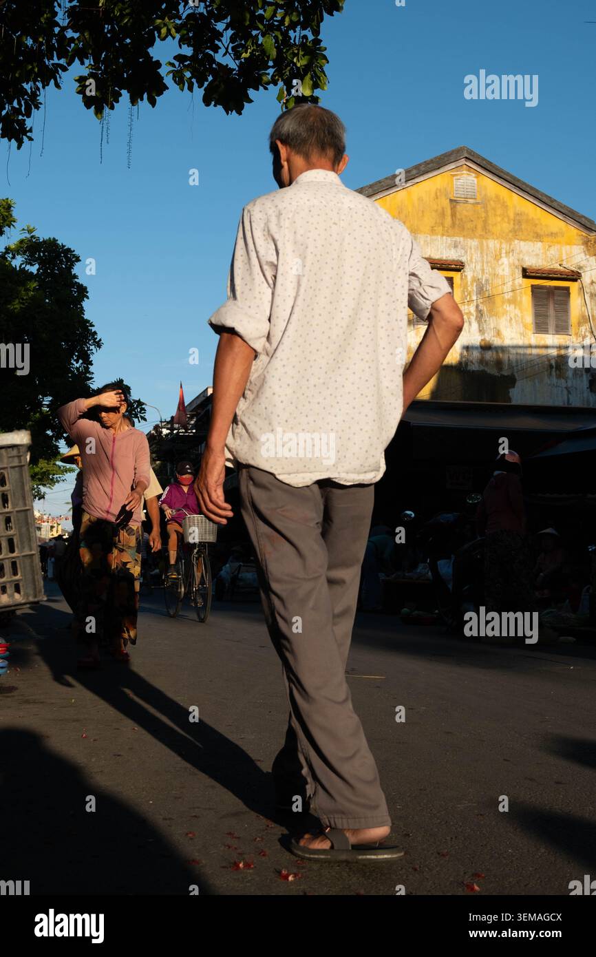 Uomo vietnamita anziano che cammina lungo una strada in una città vecchia Foto Stock