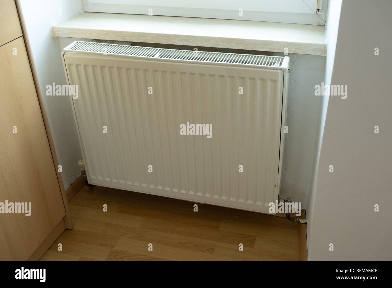 Radiatore di riscaldamento in metallo bianco sotto la soglia del finestrino. Impianto di riscaldamento centralizzato. Foto Stock