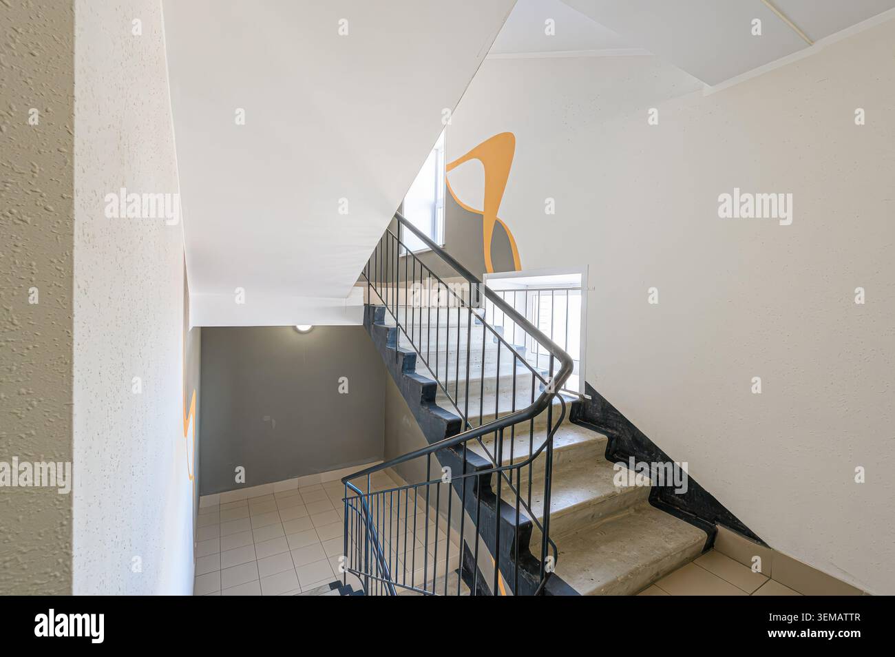 appartamento interno, luogo pubblico, vista della scalinata con gradini di cemento, ringhiera scura e pareti bianche. Un design astratto arancione è su una parete. Foto Stock