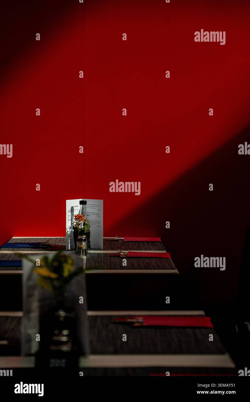 Ambiente da tavolo minimalista del ristorante con luci e ombre spettacolari contro un'audace parete rossa Foto Stock
