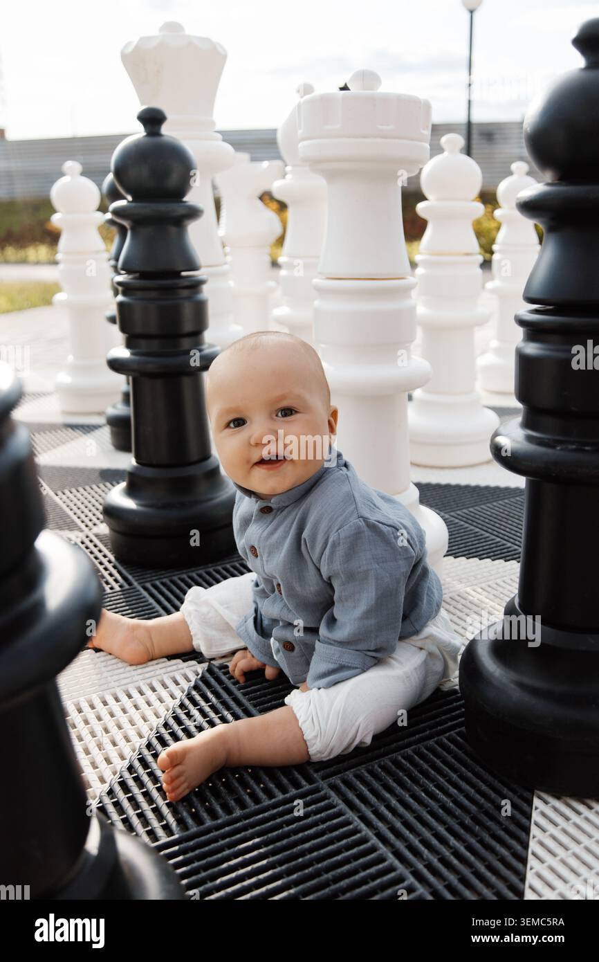 Bambino sorridente tra pezzi giganti di scacchi concetto di educazione precoce e pensiero strategico Foto Stock