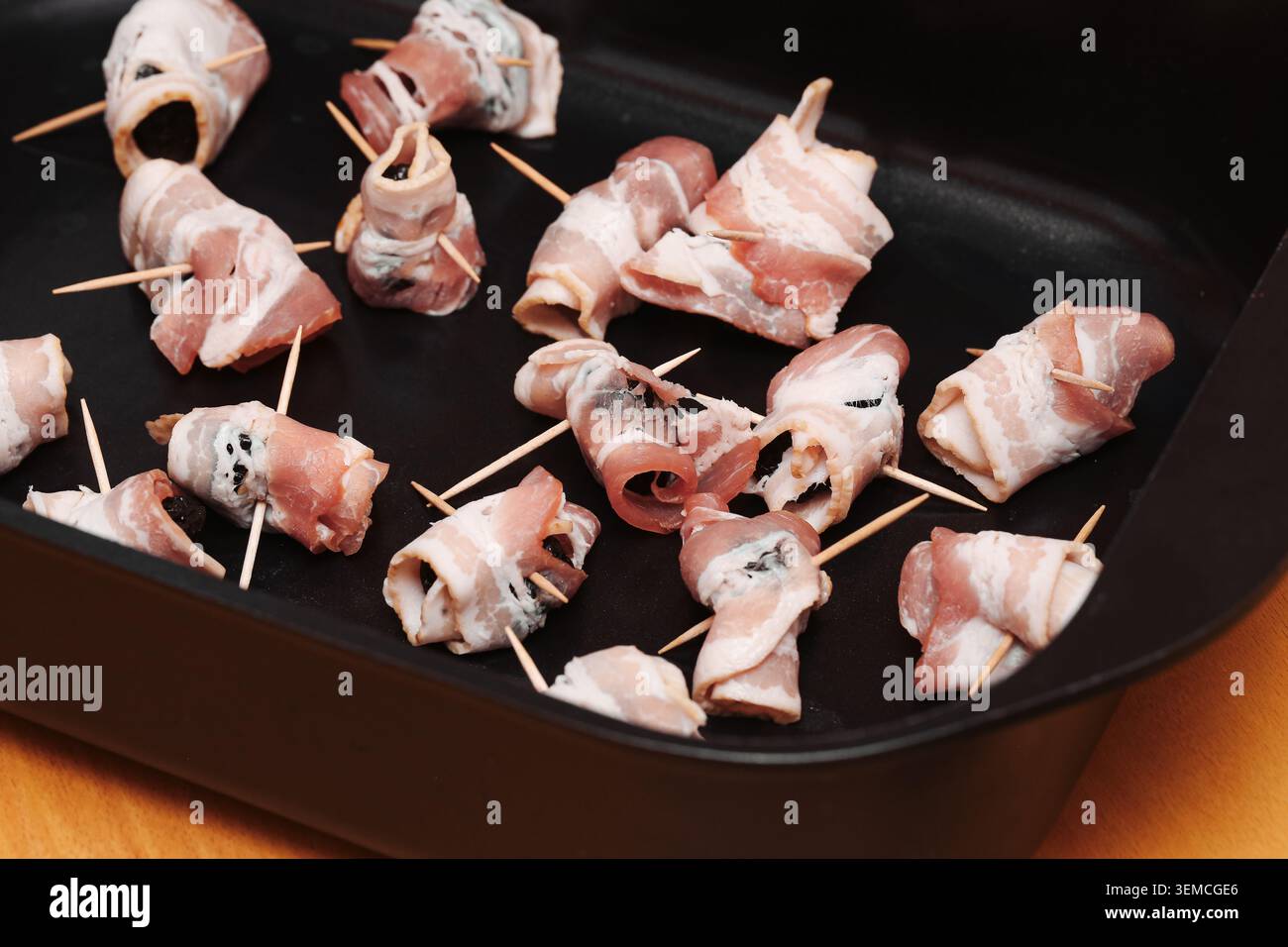 Prugne avvolte nel pancetta disposte in una teglia da forno prima della cottura. Sfondo alimentare per antipasti salati da finger food, snack per feste e pasti casalinghi. Foto Stock
