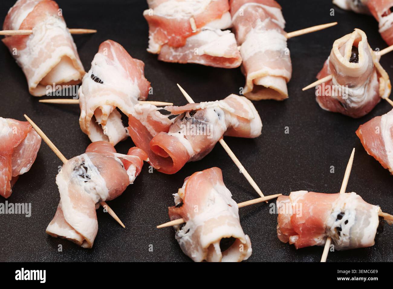 Prugne crude avvolte nel pancetto fissate con stuzzicadenti prima di cuocere. Sfondo alimentare per snack salati da festa, antipasti e cucina. Foto Stock