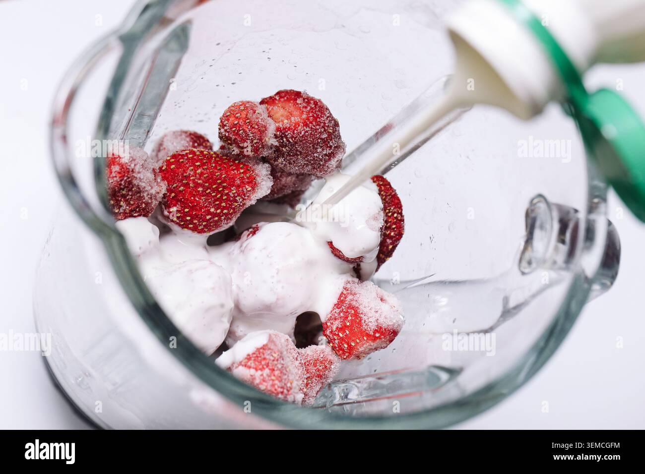Fragole surgelate frullate con latte in una caraffa di vetro. Preparazione sana di frullati per la colazione con bevande fatte in casa e ricette di frutta fresca. Foto Stock