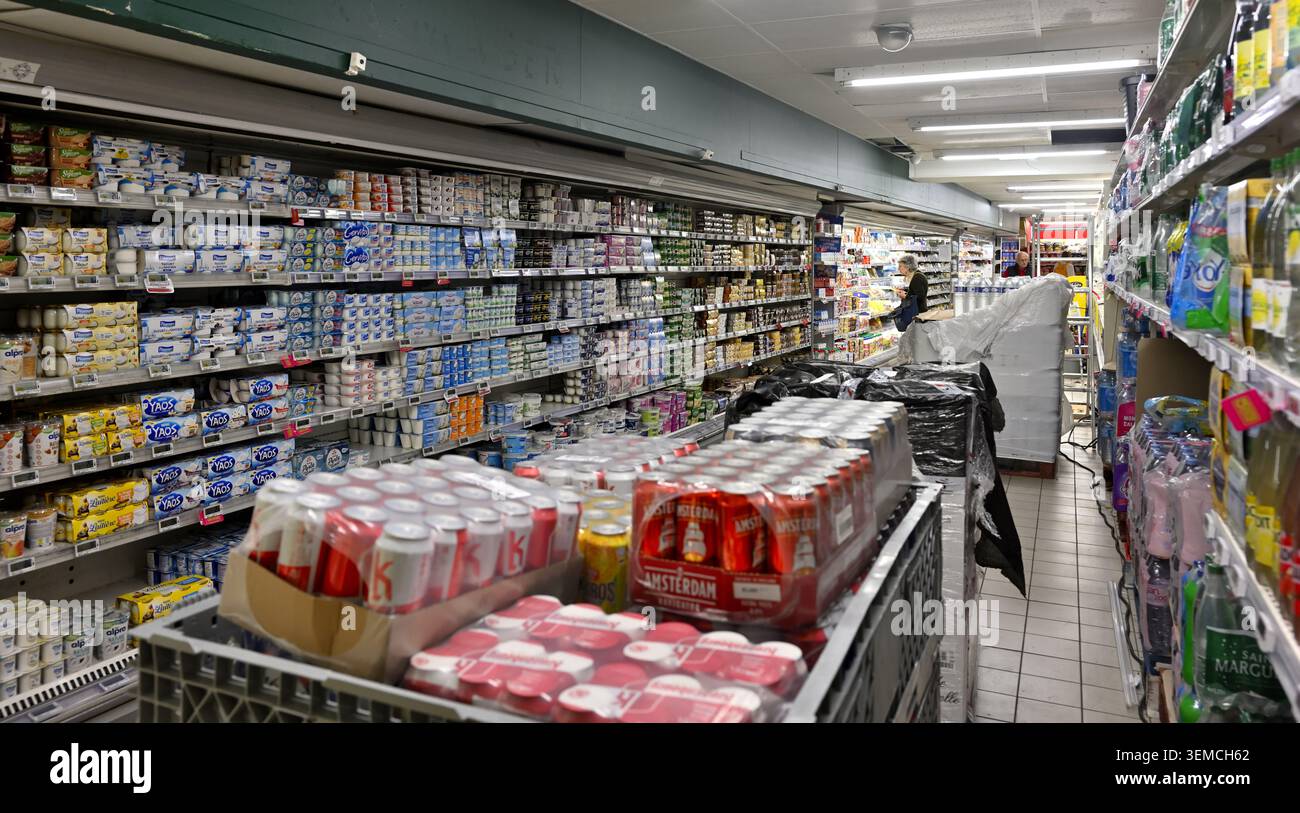 Merci impilate per rifornire gli scaffali dei supermercati con i clienti che desiderano fare acquisti nel corridoio Foto Stock