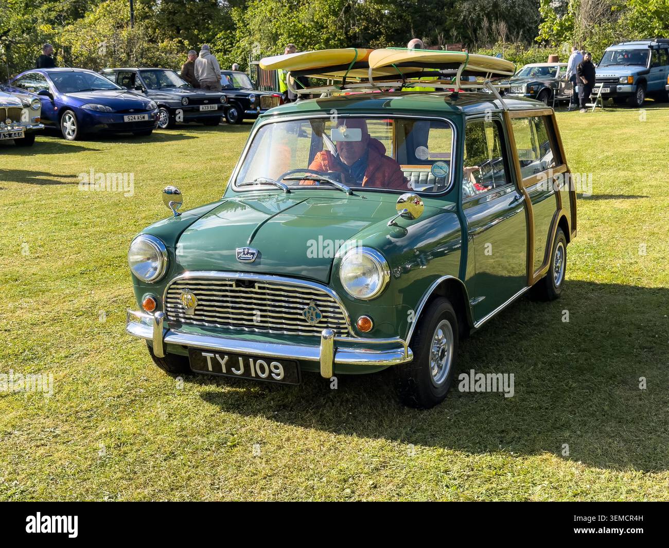 Classica station wagon verde Austin Mini Countryman con finiture in legno e tavole da surf sul portapacchi parcheggiata in occasione di una mostra all'aperto di veicoli d'epoca - Immagine stock catturata con smartphone