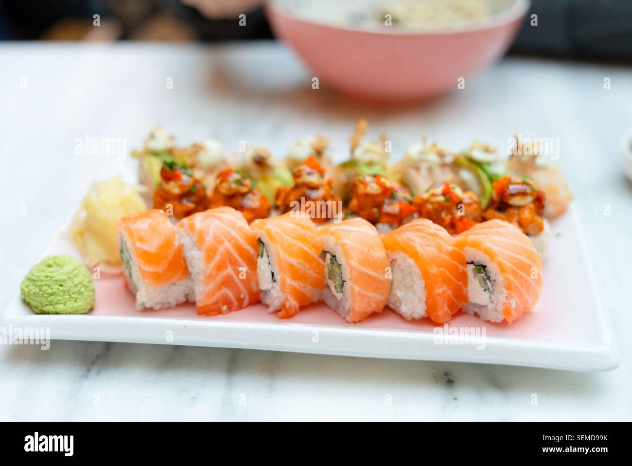 Elegante piatto di sushi su un tavolo di marmo bianco in un raffinato ristorante. Nigiri e sashimi di salmone freschi presentati su un piatto rettangolare. Ottima cucina giapponese con appetitoso stile gourmet Foto Stock