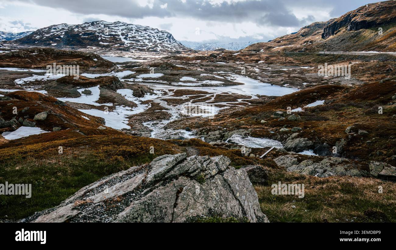 Rilascio di acqua stagionale attraverso la montagna Haukeli con campi innevati che si sciolgono e terreno esposto durante il passaggio dall'inverno nordico all'estate. Concetto di impianto idraulico Foto Stock