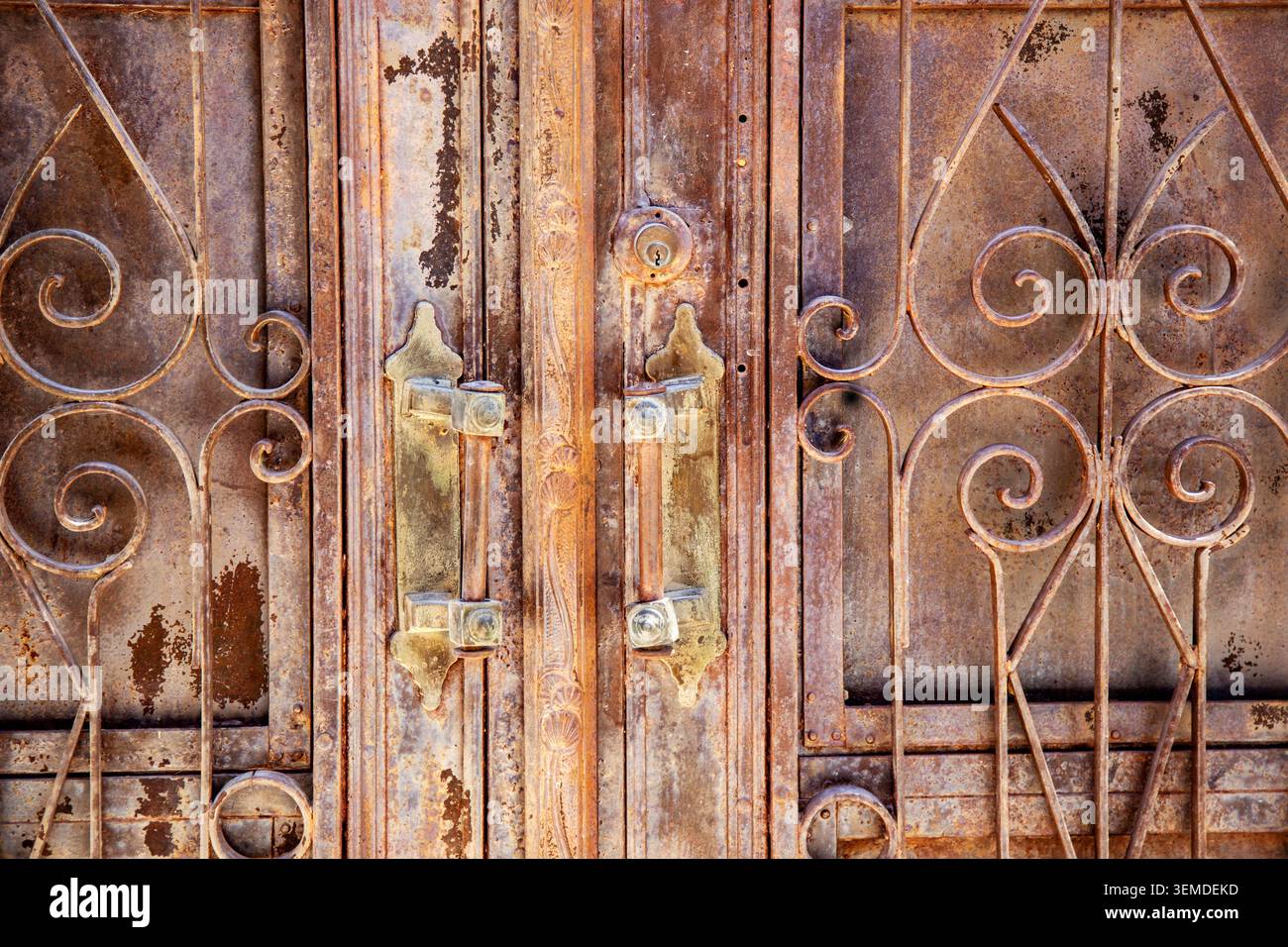 Primo piano di un cancello in ferro resistente agli agenti atmosferici con scrollwork ornati, macchie di ruggine e manici in metallo usurati, che mostrano una trama antica e patina industriale per il backgrou Foto Stock