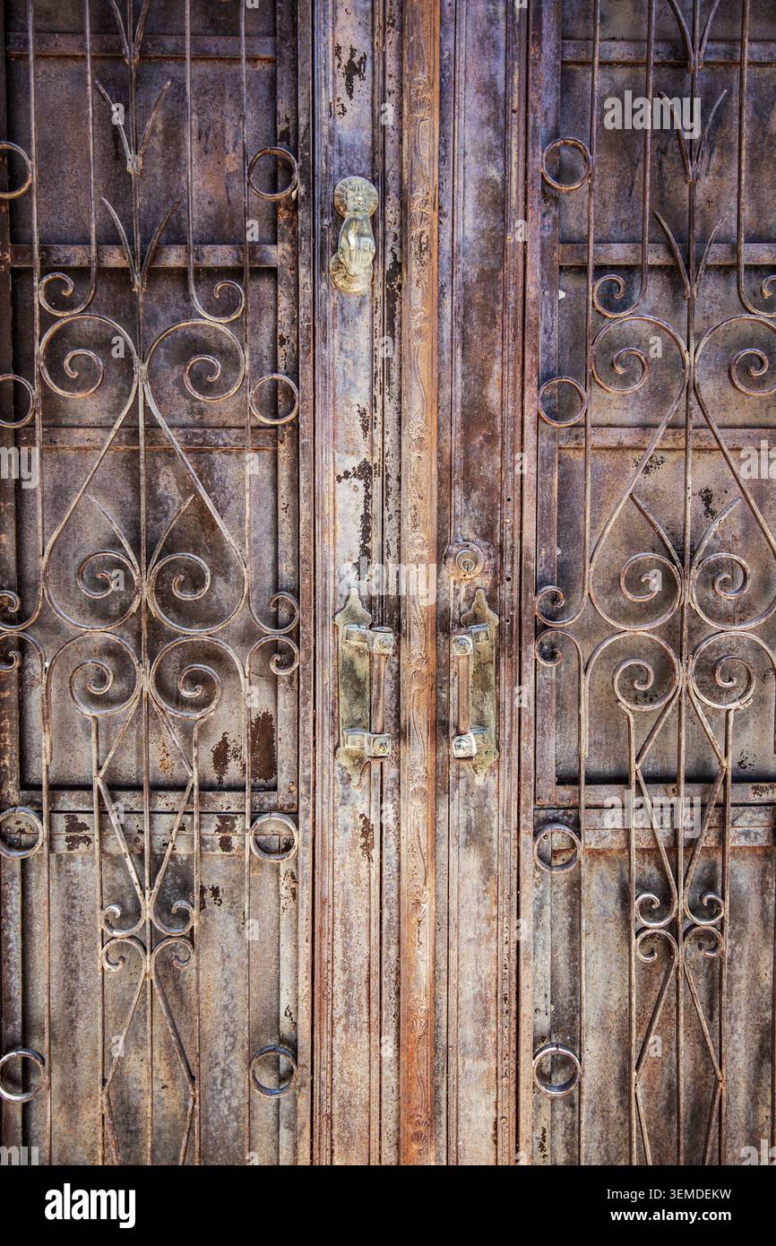 Primo piano di un cancello in ferro resistente agli agenti atmosferici con scrollwork ornati, macchie di ruggine e manici in metallo usurati, che mostrano una trama antica e patina industriale per il backgrou Foto Stock