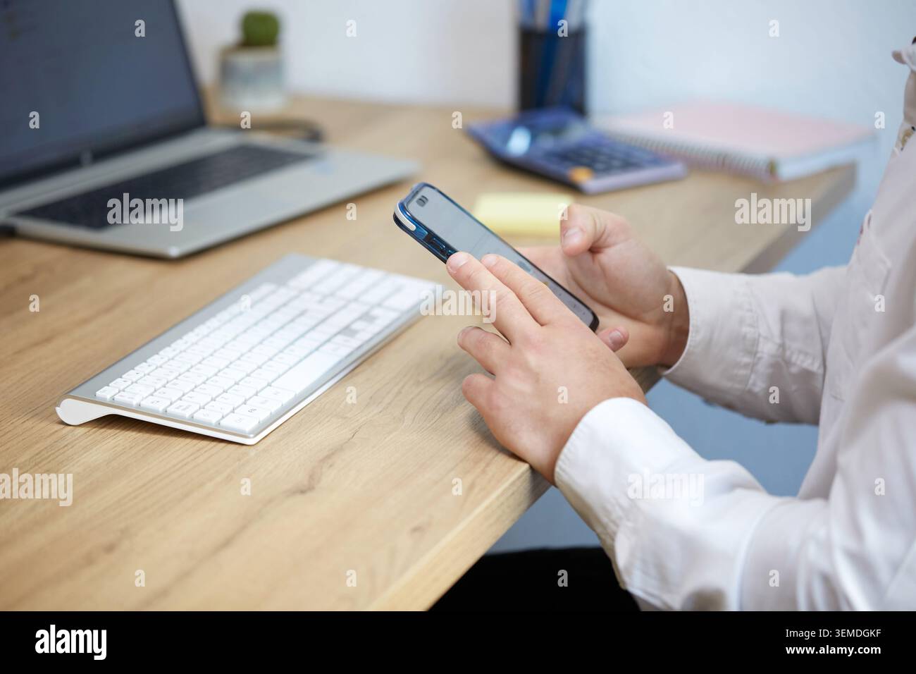 Professionisti aziendali che utilizzano uno smartphone su una scrivania dotata di laptop e tastiera, concentrandosi sull'integrazione tecnologica in un ambiente di ufficio moderno Foto Stock