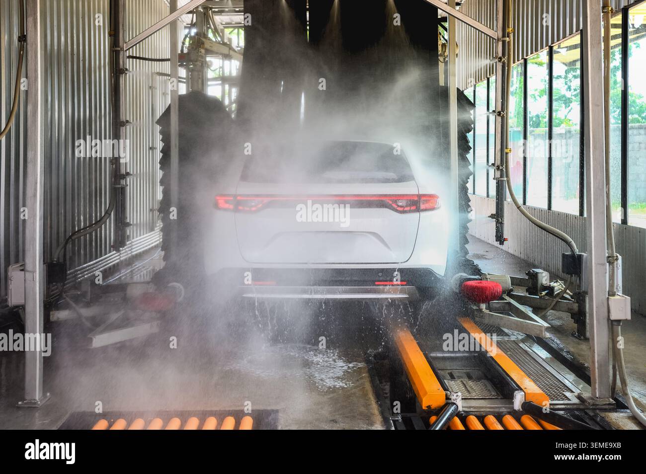 Auto bianca che passa attraverso un autolavaggio automatizzato, spruzzo automatico di acqua ad alta pressione nella lavatrice dell'autolavaggio. Foto Stock