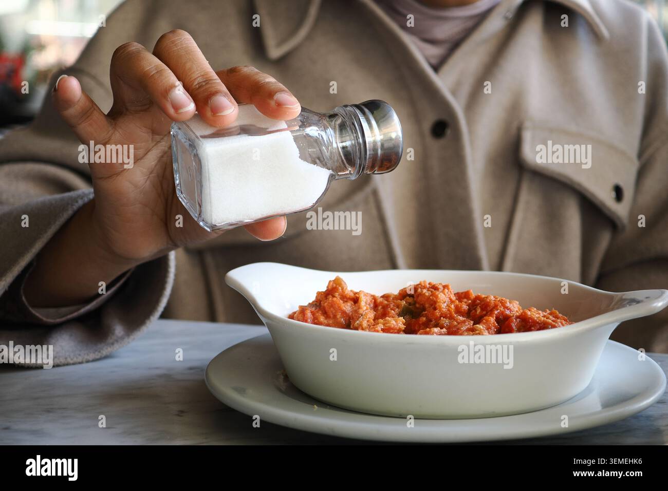 La persona aggiunge sale a un piatto a un tavolo da pranzo Foto Stock