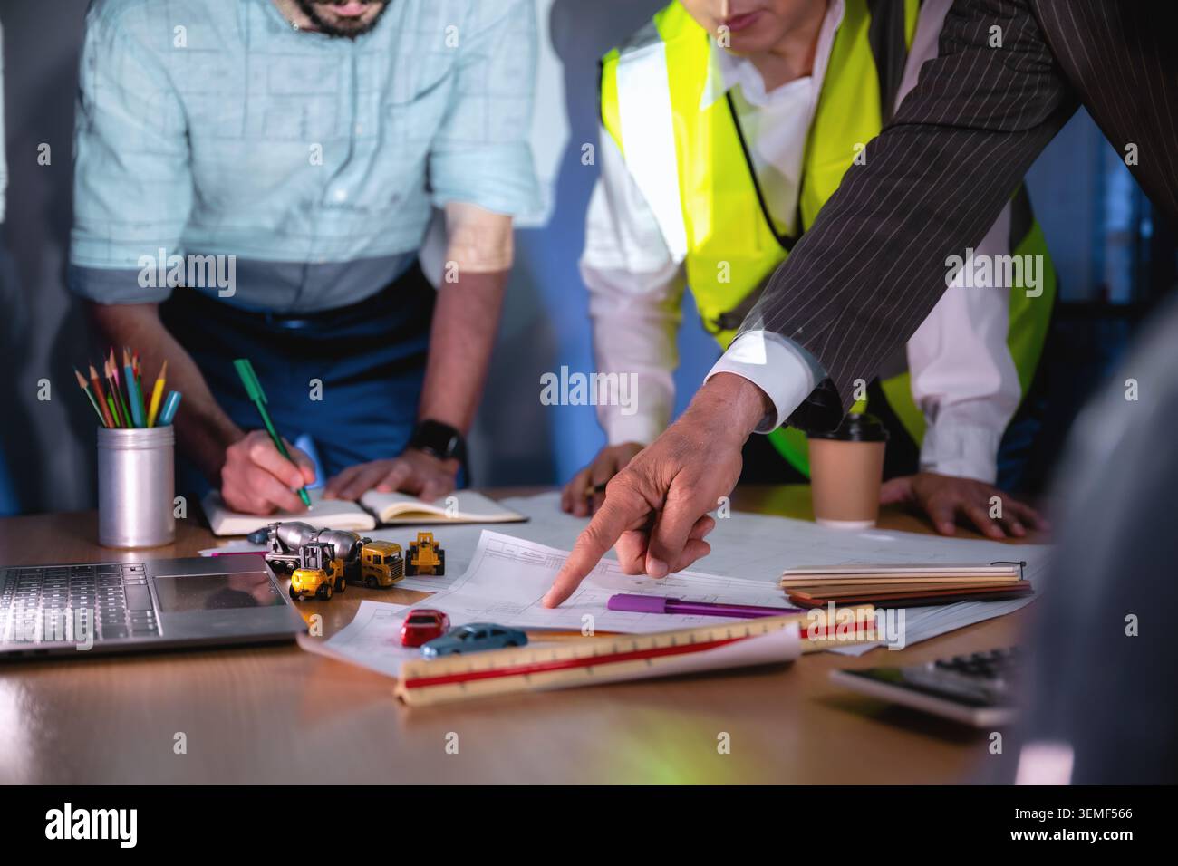 Primo piano investitore che punta il progetto di costruzione della sala riunioni, i professionisti aziendali collaborano intorno a un progetto. Uno indica t Foto Stock