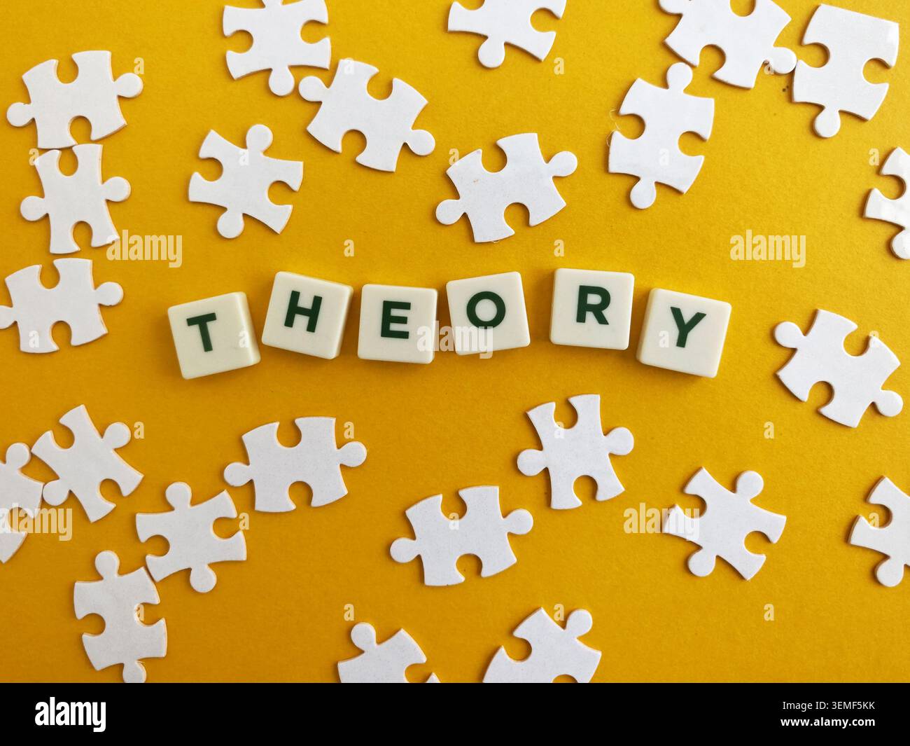 Teoria scritta con tessere di lettere, circondata da pezzi di puzzle bianchi sparsi su una superficie gialla Foto Stock