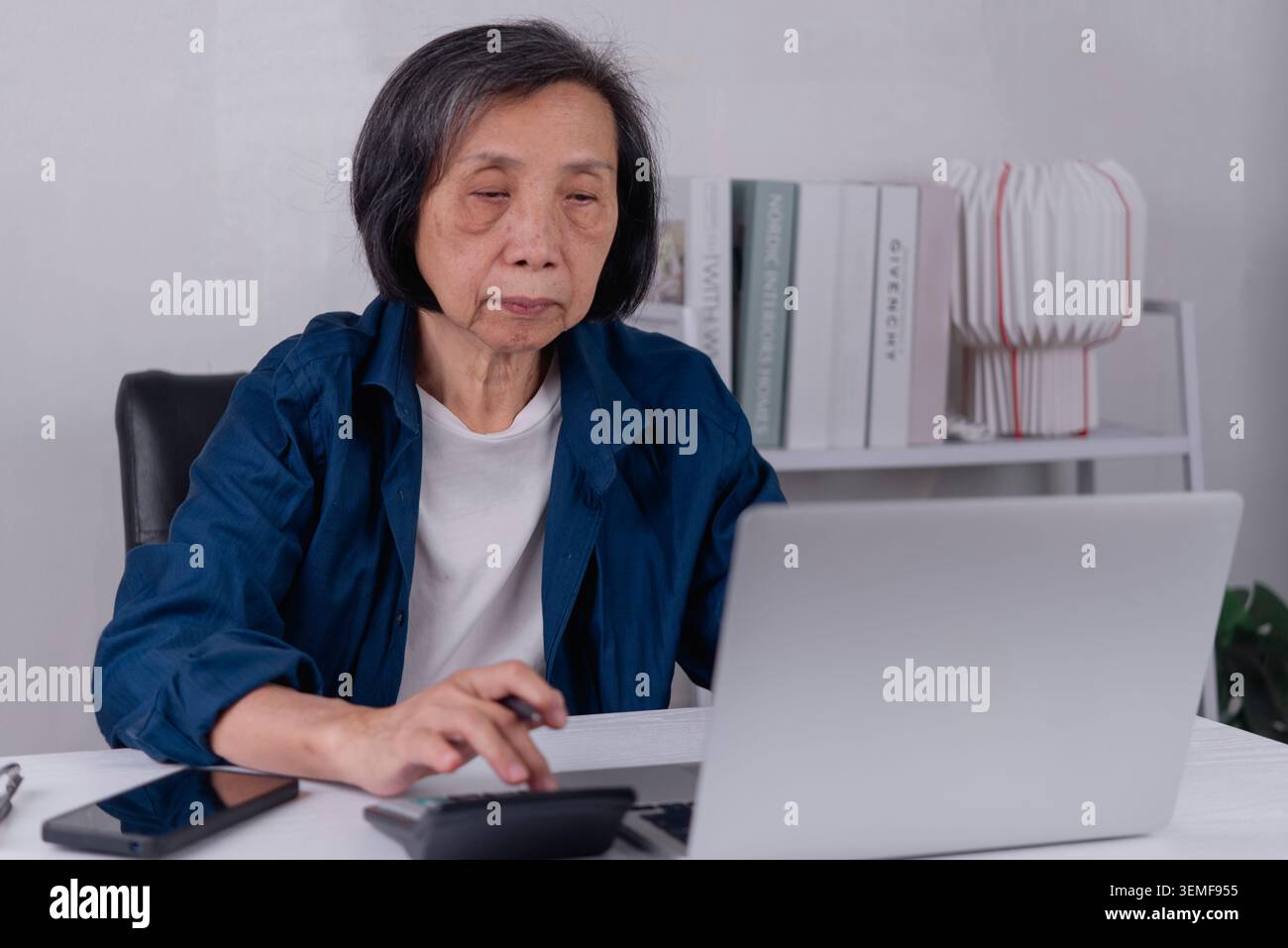 Grave donna asiatica anziana che usa la calcolatrice e il portatile con espressione preoccupata. Pianificazione finanziaria degli anziani, stress derivante dall'inflazione, costi elevati Foto Stock