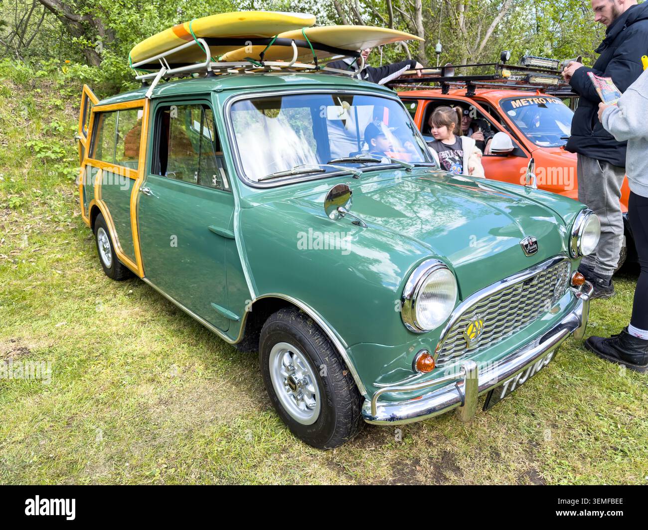 Classica station wagon verde Austin Mini Countryman con finiture in legno e tavole da surf sul portapacchi parcheggiata in occasione di una mostra all'aperto di veicoli d'epoca - Immagine stock catturata con smartphone