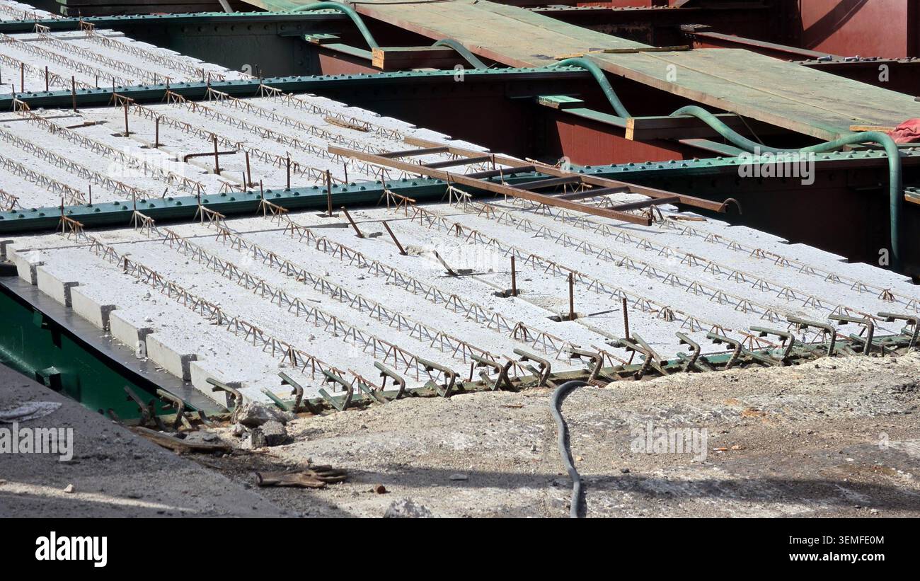 Una vista ravvicinata mostra le lastre strutturali prefabbricate in calcestruzzo con reticoli in acciaio rinforzato esposti disposti su travi a ponte in acciaio verde e marrone Foto Stock