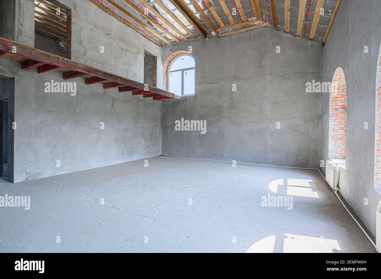 camera spaziosa e incompiuta con pareti in cemento e travi in legno. Sembra che sia in costruzione o in ristrutturazione. La luce naturale si diffonde attraverso o. Foto Stock