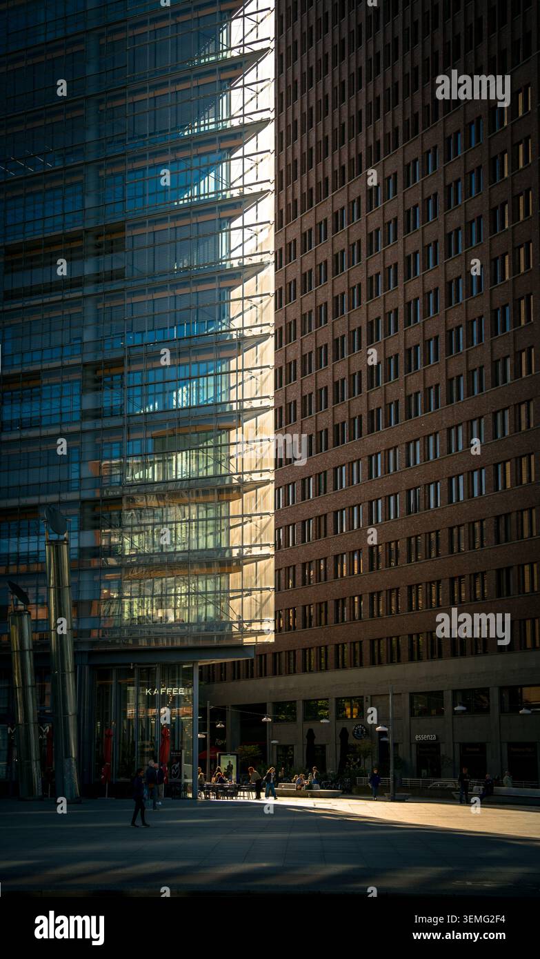 Persone che bevono caffè a Potsdamer Platz, Berlino, Germania, incorniciate da una densa architettura contemporanea e da una luce spettacolare. Foto Stock