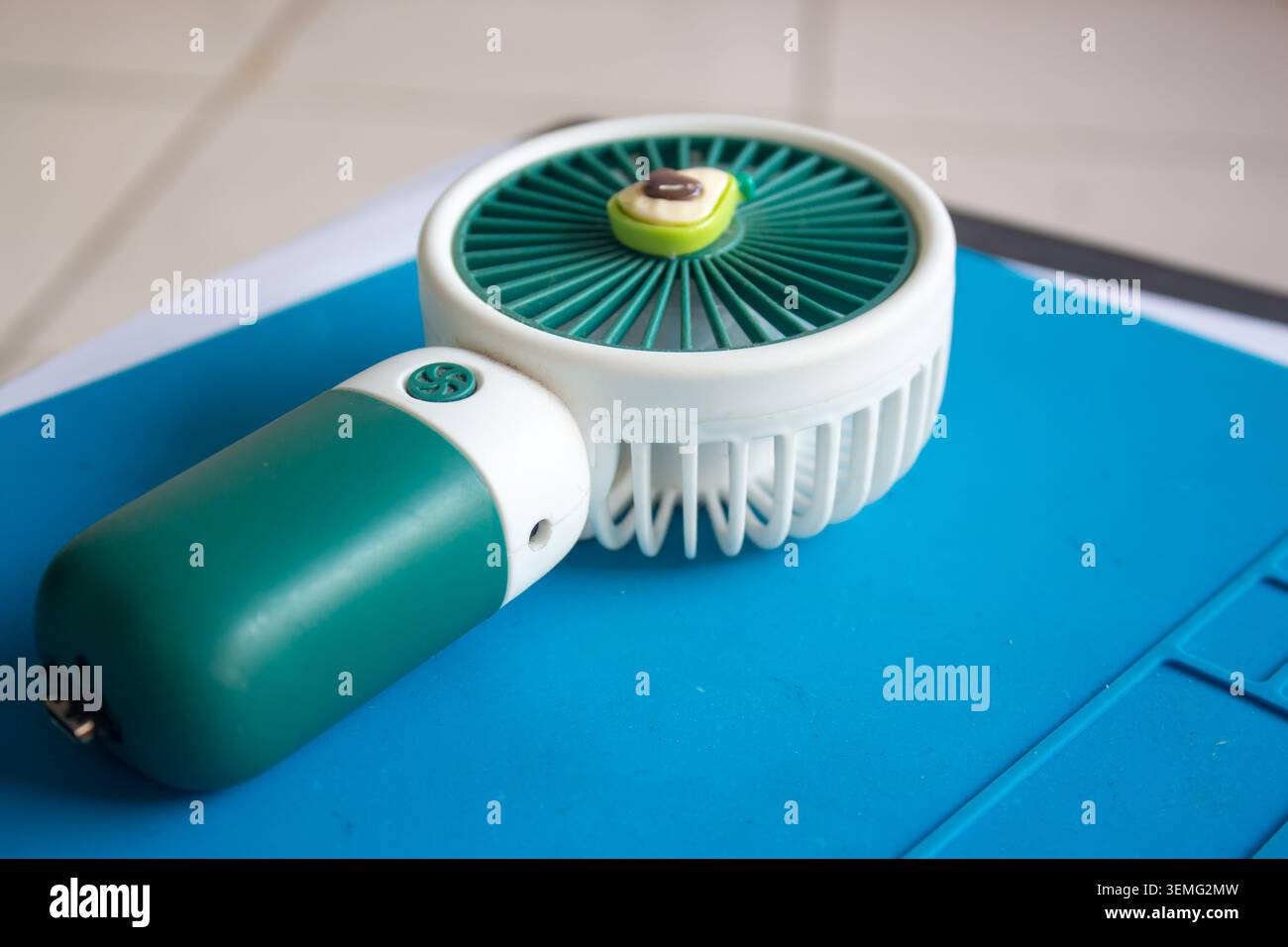 Foto ravvicinata di un mini ventilatore portatile con una graziosa decorazione avocado, posizionata su una superficie blu Foto Stock