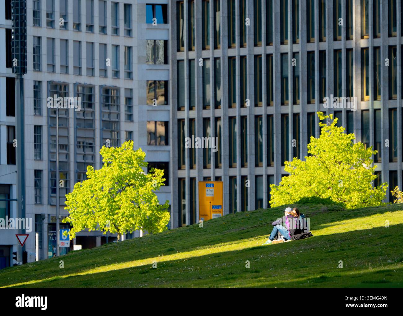 Coppia rilassante sul prato di Potsdamer Platz, Berlino, Germania, incorniciata da un'architettura contemporanea e da un fitto skyline urbano. Foto Stock